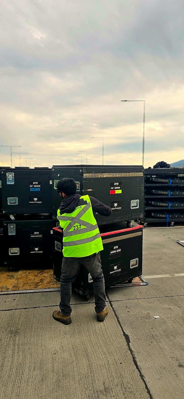 Stage hands de Kpital con chalecos moviendo cajas de equipos